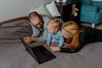 Parents with kid with computer at home on the bed