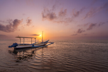 Levé du soleil avec une pirogue à balancier indonésienne sur la plage de Karang à Bali. 