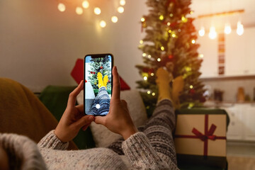 Female person lying down on sofa and takes photos of her feet in socks in front of Christmas tree....