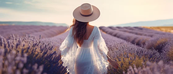 Schilderijen op glas Rear view of a young woman in a white dress and hat walking through a purple lavender field. natural background concept © Ton Photographer4289