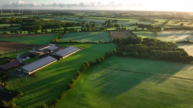 Camera panning from left to right from modern agriculture livestock farm with photovoltaic panels on the roofs of barn to foggy landcape with fields, medows in the morning haze at sunrise. 