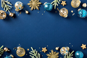 Christmas frame of blue and gold luxury Xmas balls ornaments, fir branches, confetti on dark blue background. Happy New Year greeting card template, banner mockup. Flat lay, top view, copy space.
