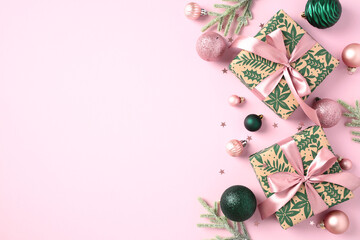Elegant Christmas greeting card template. Flat lay gift boxes with pink ribbon bow, fir tree branches, green baubles on light pink background. Top view with copy space. Xmas banner design.