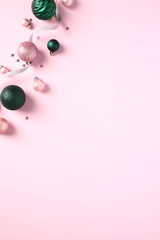 Vertical Christmas banner with green and pink Xmas balls ornament, ribbon, confetti on pastel pink background. Flat lay, top view, copy space.