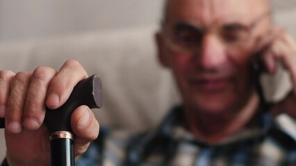 Overjoyed senior 70s grandfather sit on sofa at home laugh talking on modern cellphone, happy mature 70s man relax in living room speak have pleasant smartphone call, elderly and technology concept