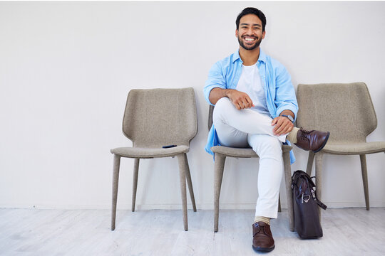 Smile, waiting and man in the office for recruitment meeting with human resources for hiring. Confidence, professional and person sitting on a chair for job interview in hallway in modern workplace.