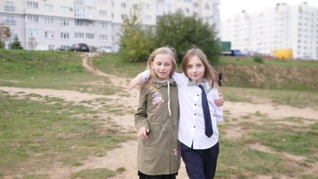 Two little girls sisters walk down the street together and hug and smile