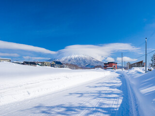 View of snowy volcano with a cap cloud beyond a heavy snowfall town (Niseko, Hokkaido, Japan)