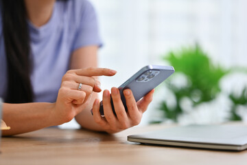 Cropped shot of woman using smartphone at desk, checking social media, communicating online
