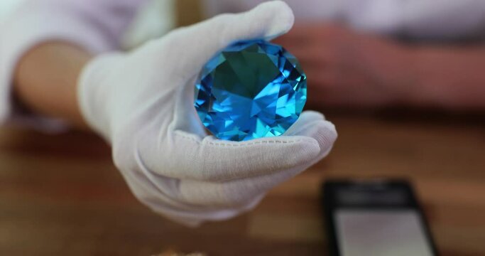 Closeup of diamond expert hands in process of grading diamonds using jewelry tools. Big beautiful blue sapphire