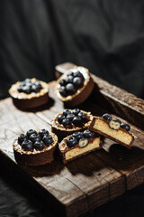 Chocolate tartlets decorated with blueberries on a dark wooden background. Beautiful portion cakes for the holiday table. Dessert with fresh blueberries.