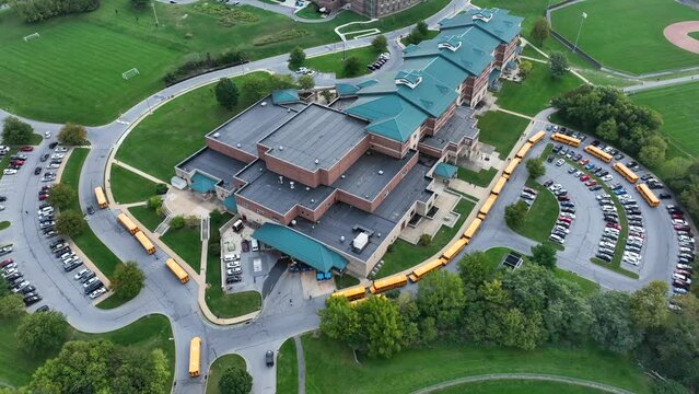 Large American high school with lines of yellow school buses waiting to pick up students from school and drop off at houses. Aerial establishing shot.