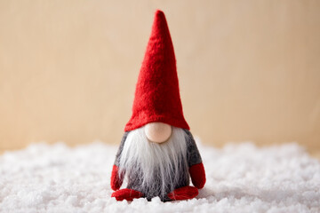 christmas, decoration and winter holidays concept - close up of gnome toy on artificial snow on beige background