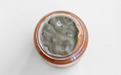 Open jar with sweet jam and mold on a white background. Mold in a jar of raspberry jam. Hazardous to health.  - obrazy, fototapety, plakaty
