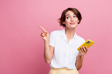 Portrait of positive clever girl with brunette hair look directing at promo empty space hold smartphone isolated on pink color background - obrazy, fototapety, plakaty