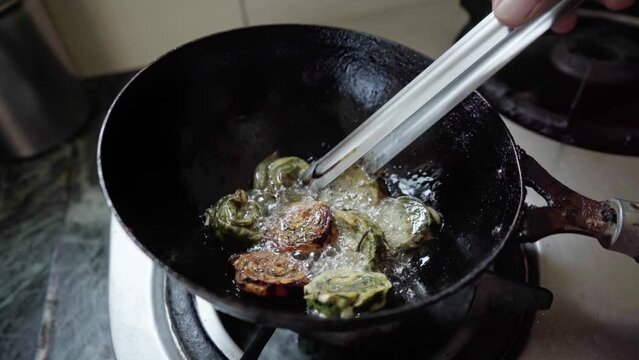 indian woman deep frying bhajiya or alu vadi in oil. alu vadi patra or ptrode maharashtrian and gujarati snack. 