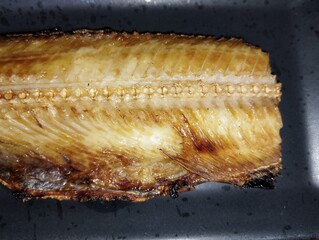 焼き魚ホッケが黒い皿の上にのっている
