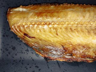 焼き魚ホッケが黒い皿の上にのっている