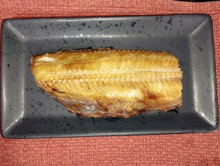 焼き魚ホッケが黒い皿の上にのっている