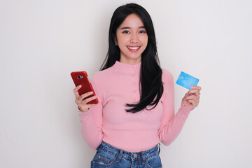 Young Asian woman smiling while holding mobile phone and blank credit card