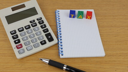 The word Tax written with wooden blocks and notepad and calculator on the table, copy space.