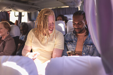 Albino man talking to his black colleague, using smartphone, inside the bus. - Powered by Adobe