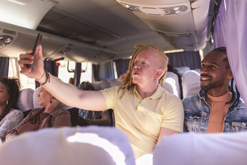 Homem albino tirando uma selfie com seu colega durante trajeto de onibus.