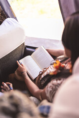Young indigenous woman reading a book during a bus ride. Over-the-shoulder view.