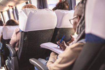 Mulher negra de meia idade fazendo anotacoes em um caderno durante uma viagem de onibus. Vista...