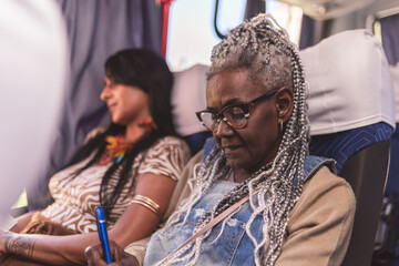Portrait. Senior black woman with stylish afro hair, taking notes in a notebook during a bus ride.