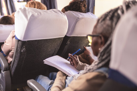 Mulher negra de meia idade fazendo anotacoes em um caderno durante uma viagem de onibus. Vista sobre o ombro.