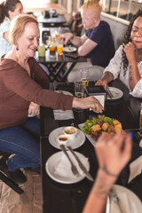 Obraz na płótnie Canvas Mulher senior comendo petiscos com amigos em um bar ao ar livre.