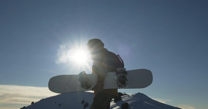 Snowboarder walks along snow mountain. Tired after long way up tourist with snowboard looks forward to descent from steep mountain. Love for active sports, wandering along highest point of snow slope.