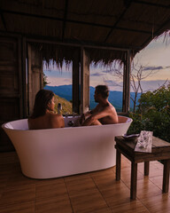 a mixed couple of men and women in a bathtub looking out over the mountains of Chiang Rai Northern Thailand during vacation. Outdoor bathroom, bathtub during sunset