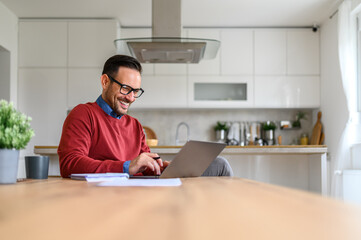 Smiling businessman with note pad and documents on desk working over laptop in home office