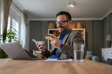Low angle view of male professional paying with credit card over smart phone while sitting at desk