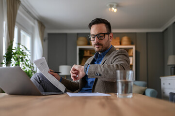Low angle view of confident businessman checking time on wristwatch while working in home office