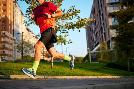 Cropped image of athletic man in sportswear and running shoes training, running outdoors on early summer morning. Concept of sport, active and healthy lifestyle, competition, dynamics