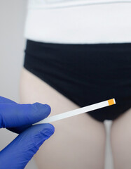 Bacterial Vaginosis. Vaginal pH. Girl shows sticks for measuring acid-base balance of genital organs. Self-diagnosis. Normal acidity level shown in colors and must be compared with the standard