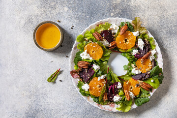 Christmas appetizer. Christmas wreath salad with beetroot, tangerines, feta cheese and pecans on the festive table. View from above.