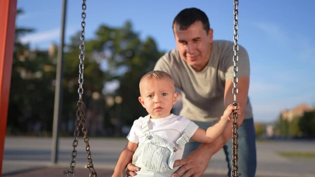 a happy family. dad pushes baby on swing. city . happy child swinging on a swing. fun time. child rides form content lifestyle