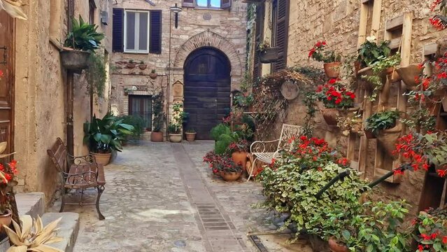 romantic Italian street 4K. Quiet floral alley in Spello, Umbria. Traditional stone houses with flower pots and Empty ornate metal benches. Italy travel footage