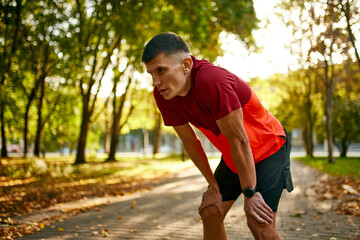 Taking a rest. Man in sportswear, running athlete in sportswear leaning on knees and resting on the...