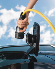 Female hand charging electric car with blue sky, photo from below