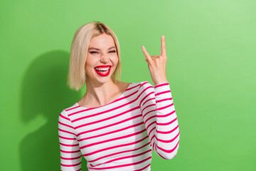 Photo of optimistic cool woman with bob hairdo dressed striped shirt fingers showing horns symbol isolated on green color background