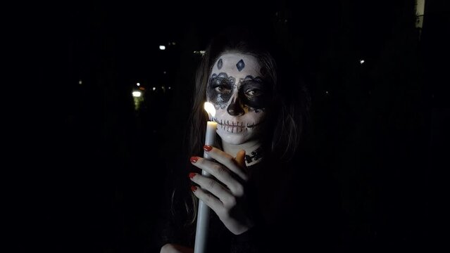 girl with sugar skull holds burning candle hands dark street. All Saints' Day holiday concept