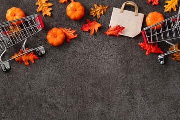 Autumn shopping design concept background with shopping cart, maple leaves and pumpkin.