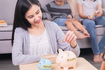 Asian mother put coins in piggybank saving money for medication and education for children lifestyle concept, well organize planning of single mom with two kids for finances and house expenses