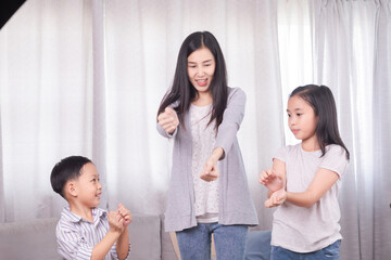 Happy family single mom dancing together with sibling children in living room at home, cheerful mother playing with little boy and girl kids exercise with music, healthy family bonding relationship