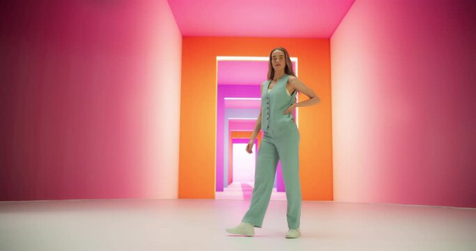 Tracking Low Angle Portrait of a Fashionable Young Woman Performing a Catwalk in a Colorful Neon Studio. Stylish Female Walking Confidently In and Out of a Bright Lit Room